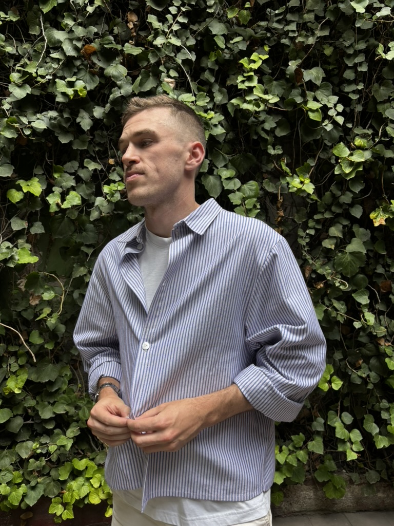 Reis wearing his blue-and-white striped button-down with rolled sleeves in front of an ivy-covered wall.